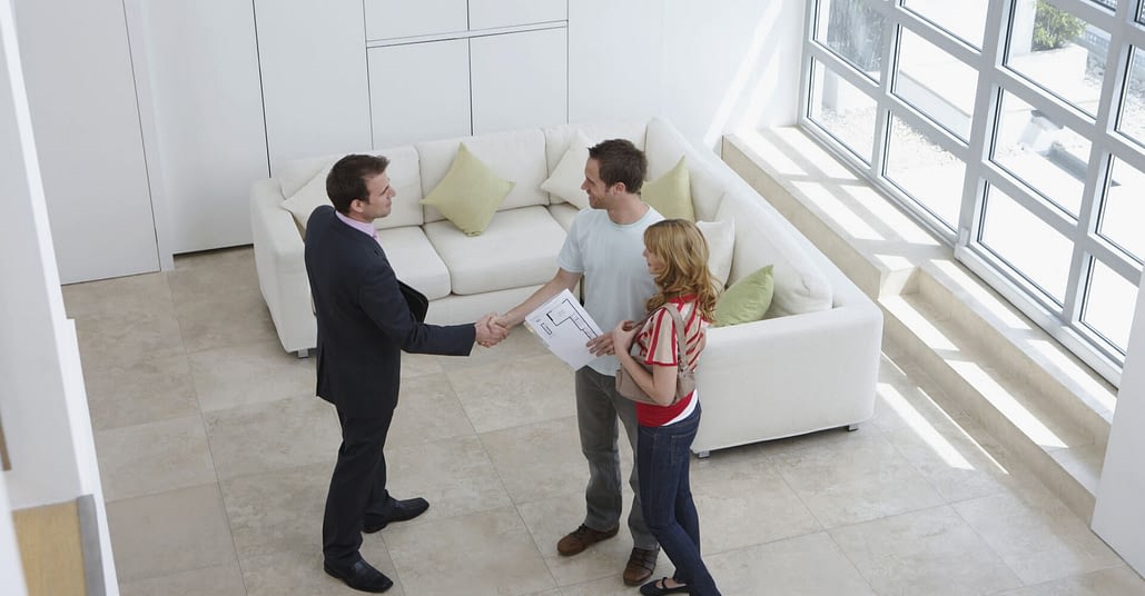 Elevated view of a male real estate agent shaking hands with a man by woman in new home